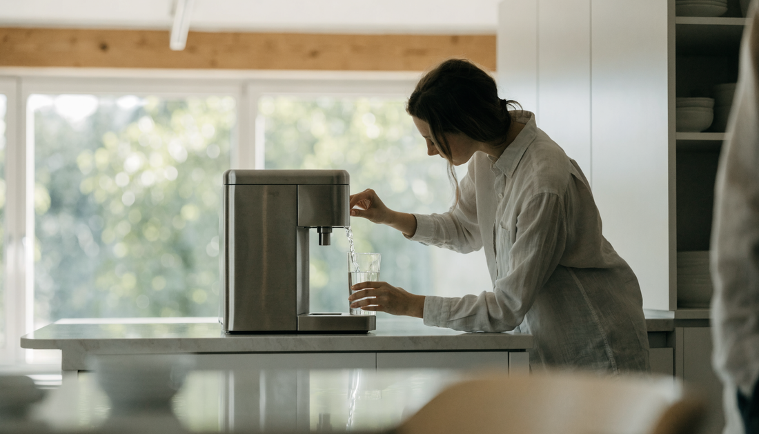 Medarbejder fylder glas ved vandautomat til kontor i lyst kontormiljø