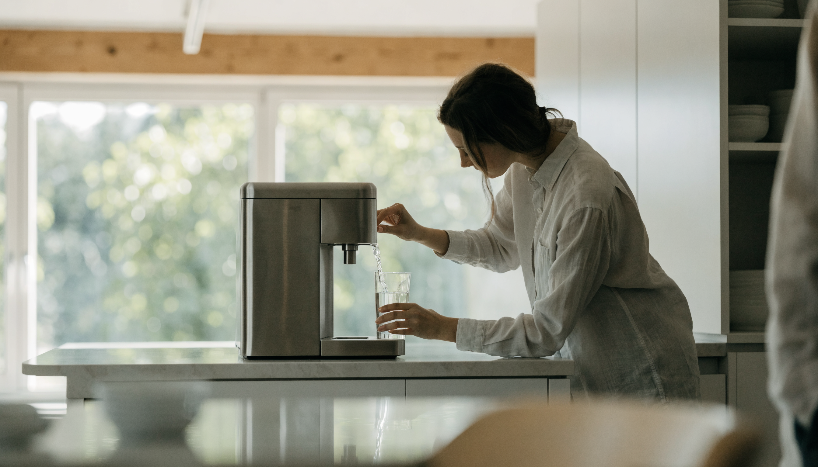 Medarbejder fylder glas ved vandautomat til kontor i lyst kontormiljø